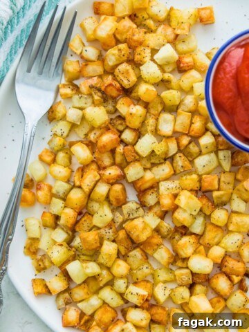 A plate of cooked hash browns with a fork on it and a side dish of ketchup on the other side of the plate.