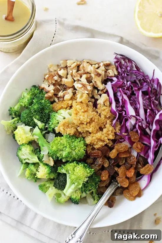 A white bowl filled with Crunchy Broccoli Quinoa Salad and a jar of dressing to the side.