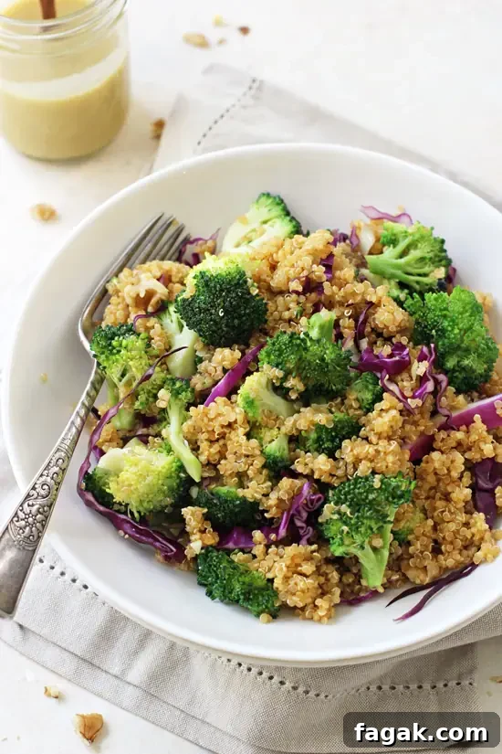 Side angle view of Broccoli Quinoa Salad in a bowl with a fork and a jar of dressing in the background.