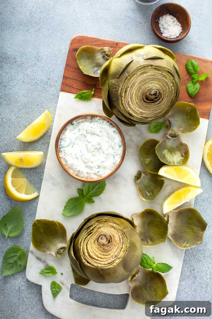 two artichokes with dipping sauce in a small bowl over a marble board