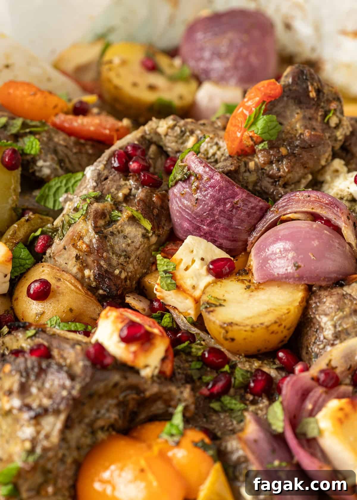 closeup: roasted kleftiko in a pan with potatoes, onions, and fresh parsley and pomegranate seeds on top