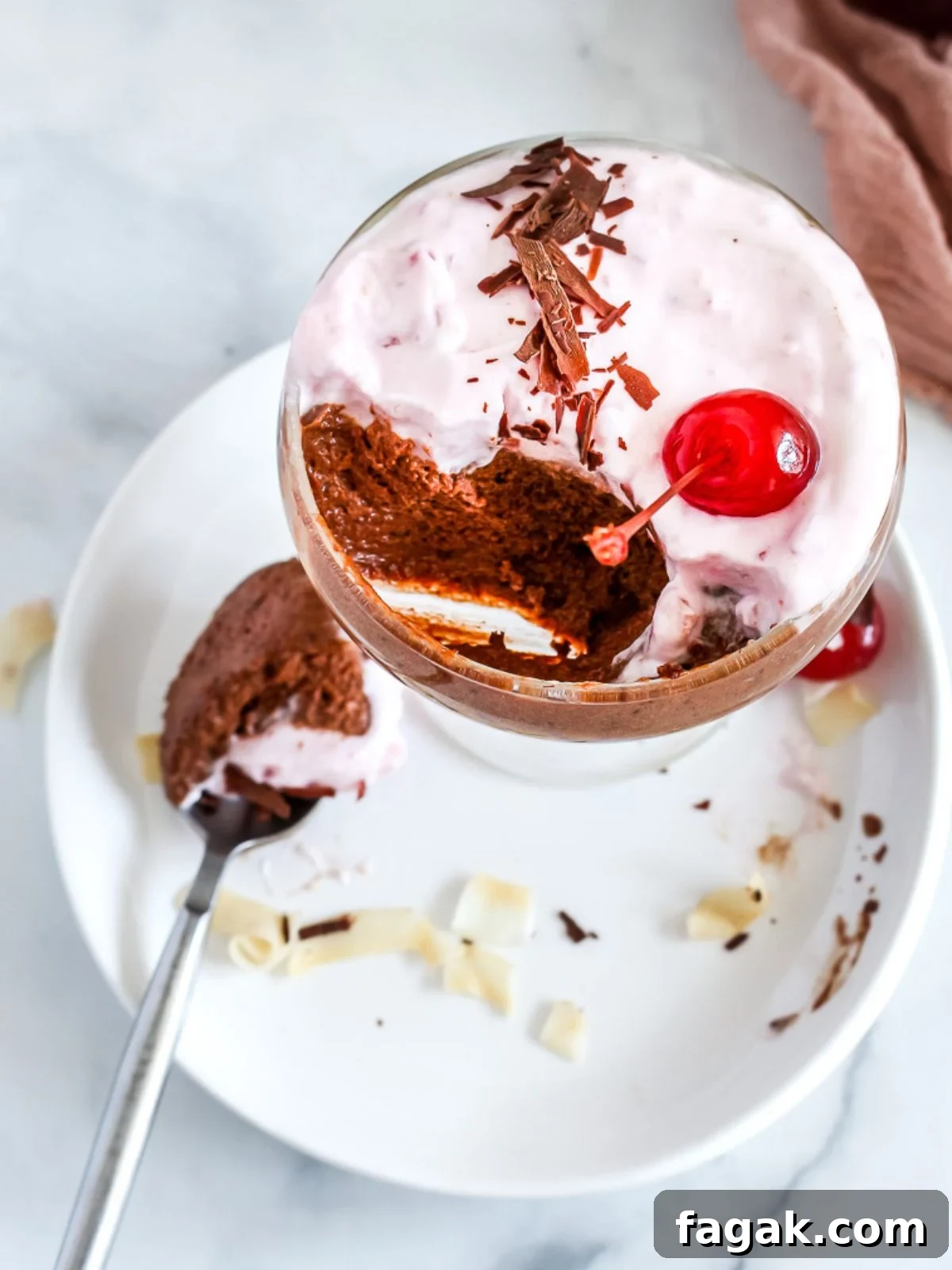 A cup of coconut mousse  with chocolate topped with cherry and shaved chocolate.