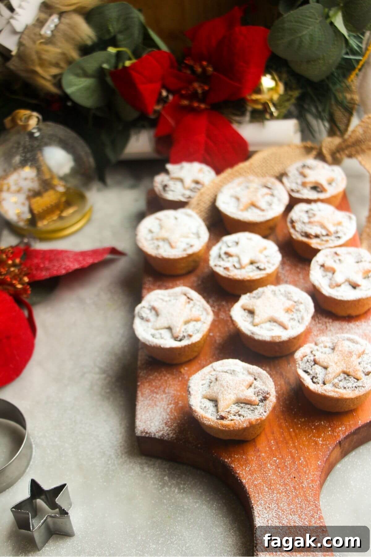 Icing sugar dusted Christmas fruit mince pies on a small wooden board with red and gold decorations in the background.