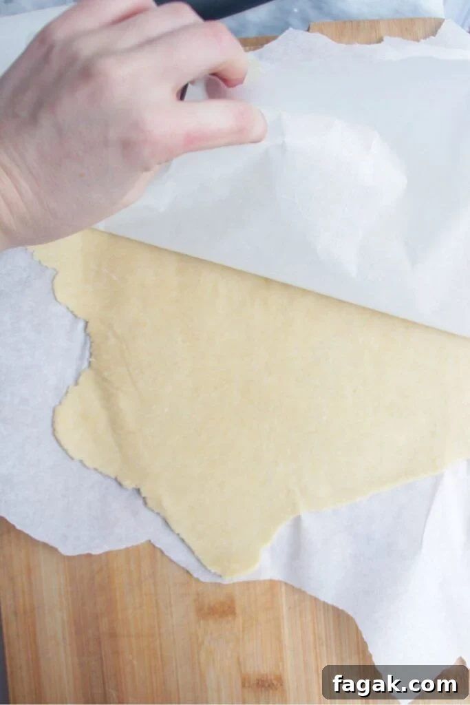 Hand peeling back baking paper to reveal rolled out pastry underneath.