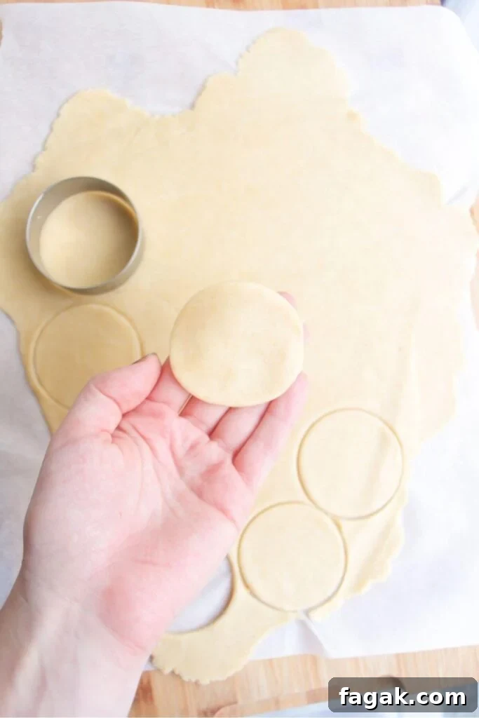A hand holding up small pastry circle with more pastry in the background.