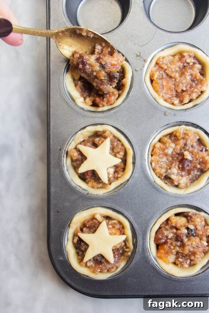 A spoon filling pastry case with fruit mince in a small muffin tin.