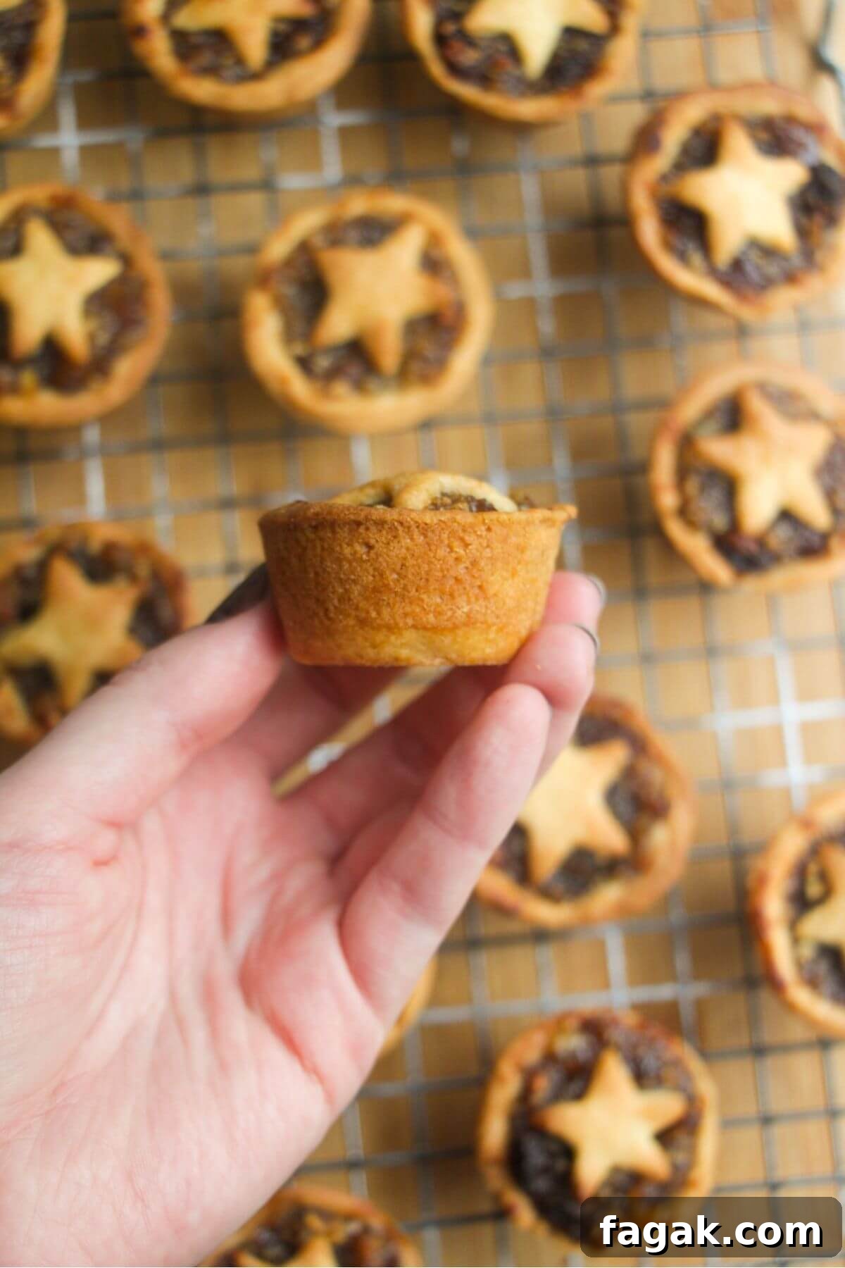 A hand holding up a fruit mince pie, showing the side of the pie.