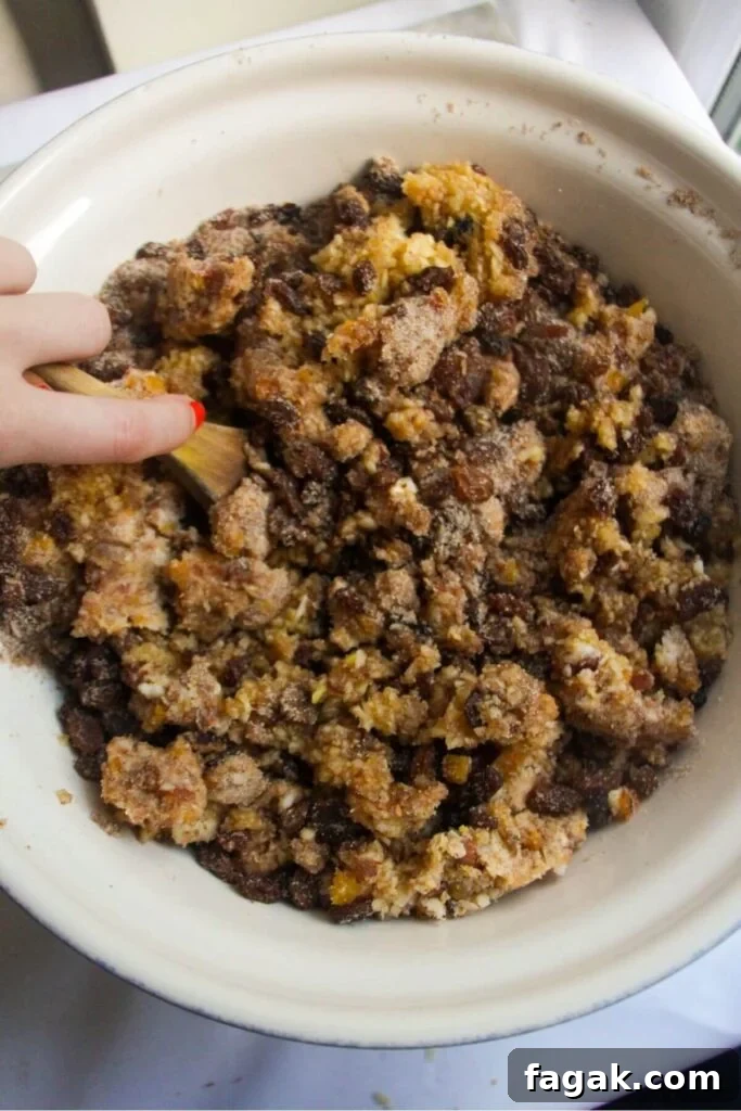 Hand holding a wooden spoon and stirring Christmas fruit mince in a large white bowl.