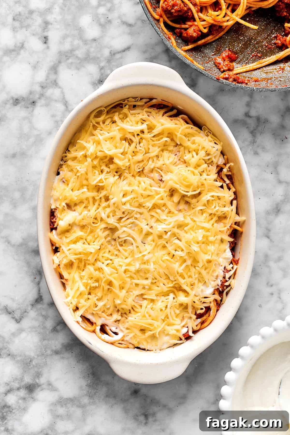 Adding a layer of shredded cheese on top of spaghetti in a 9x13 dish.