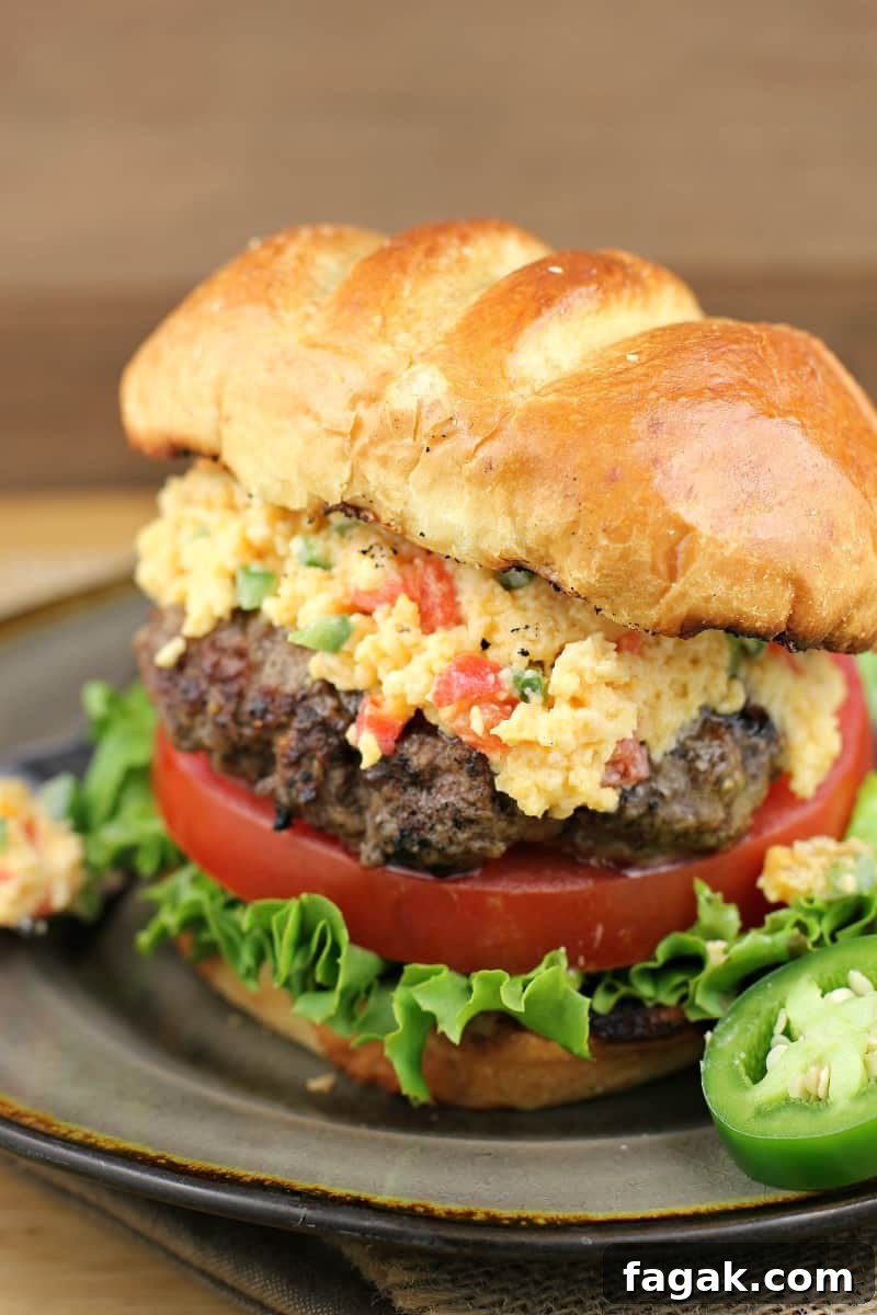 close view of assembled jalapeno pimento cheese burger on a plate, sliced jalapeno on the side