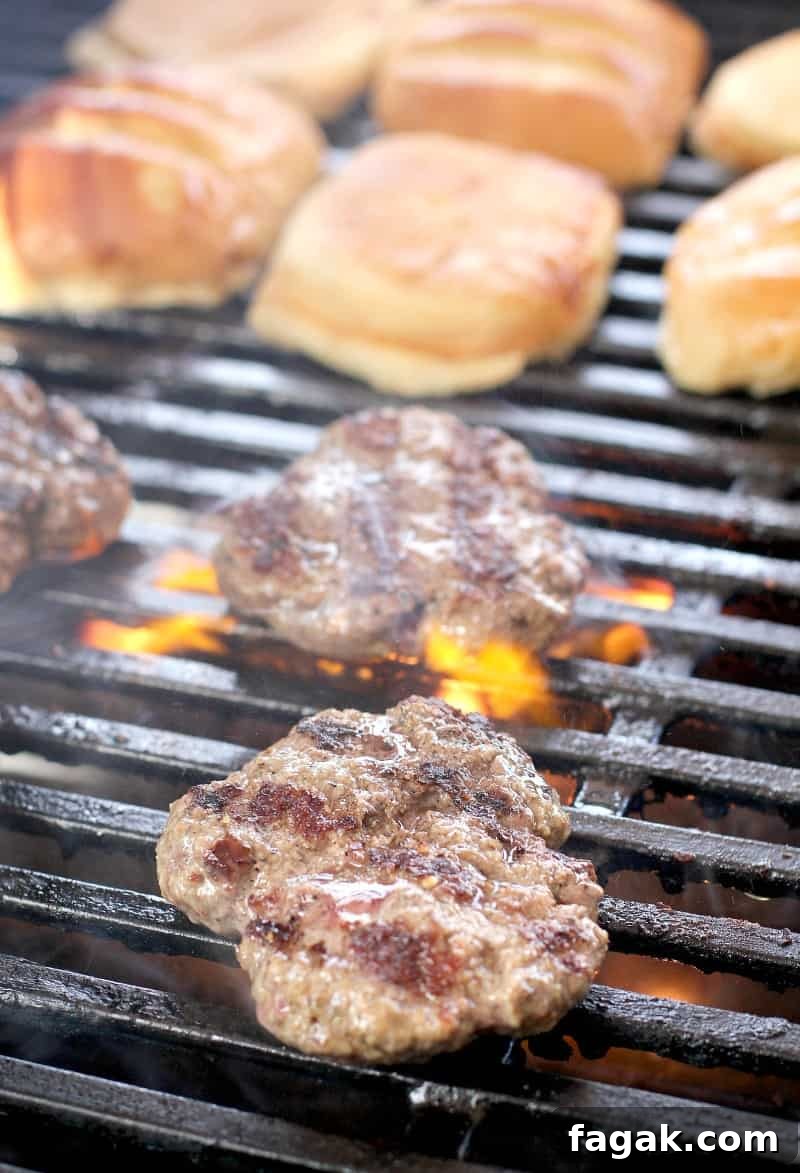hamburgers cooking on a grill, buns toasting in the background