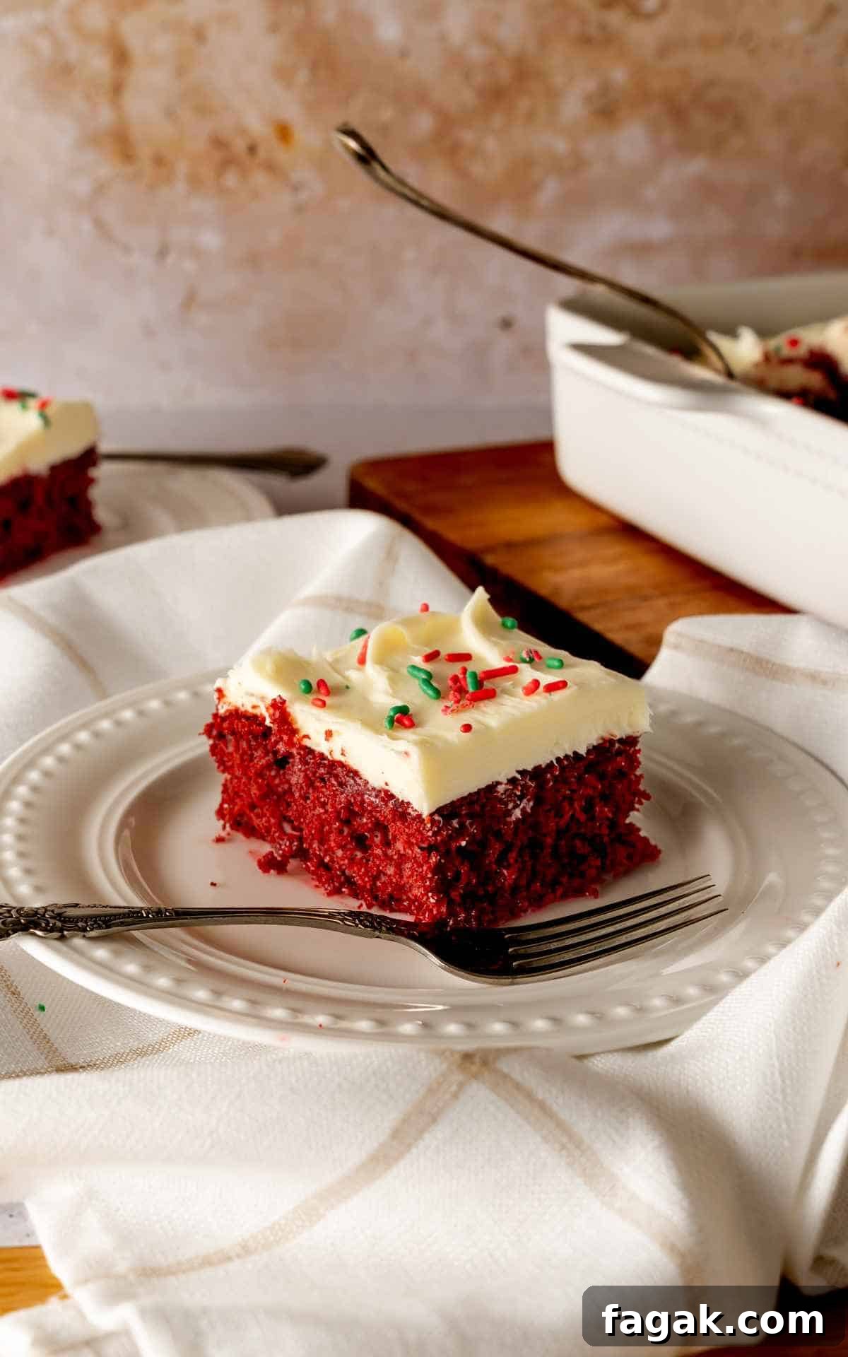 A slice of red velvet poke cake with a fork on a decorative white plate.