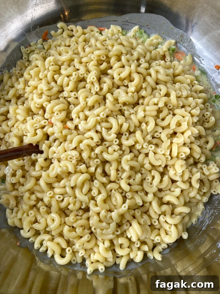 Cooked macaroni being stirred into veggie and dressing mixture
