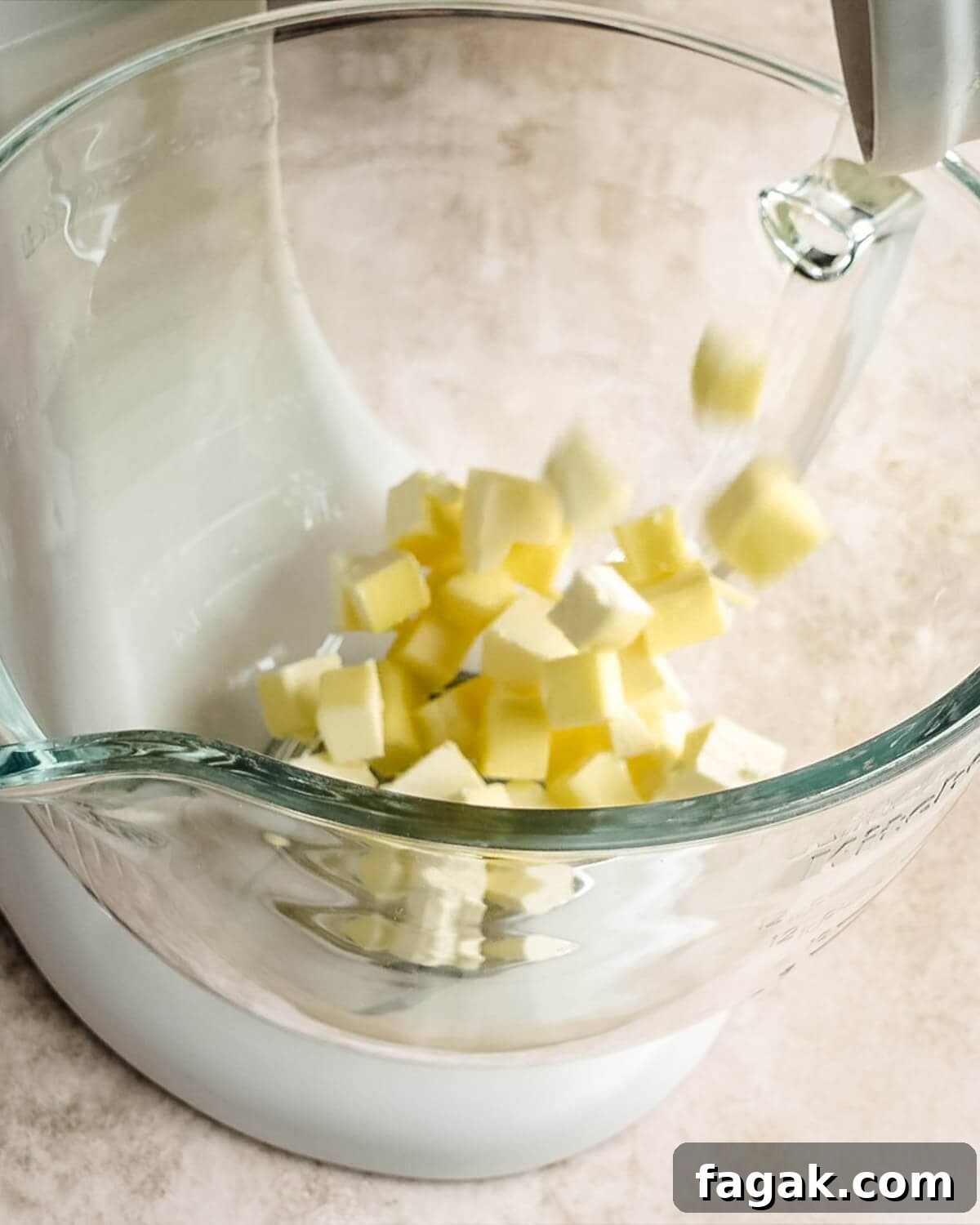 Cubed butter added to a glass Kitchenaid mixing bowl.