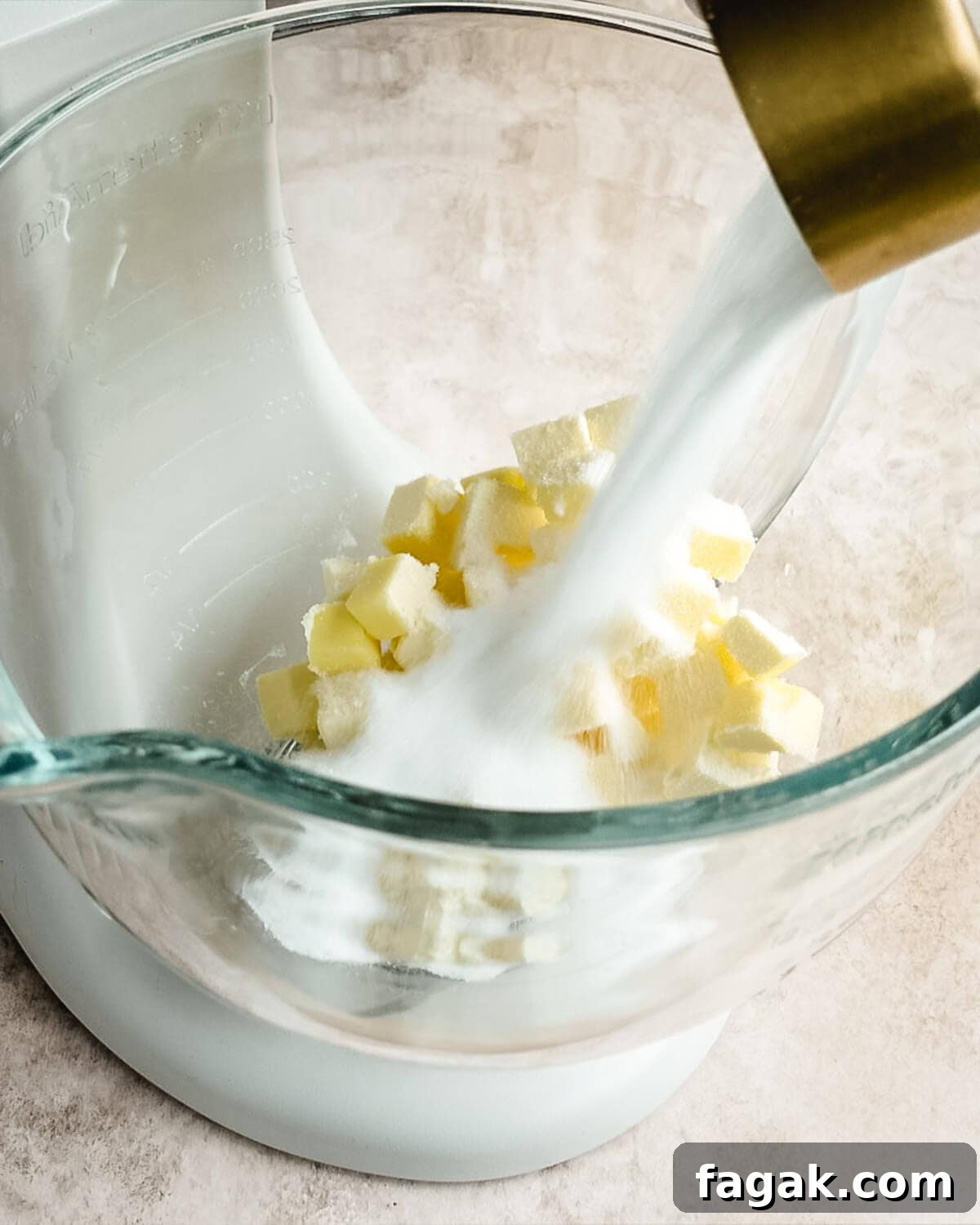 Cubed pieces of butter in a mixing bowl with sugar being added to the bowl.
