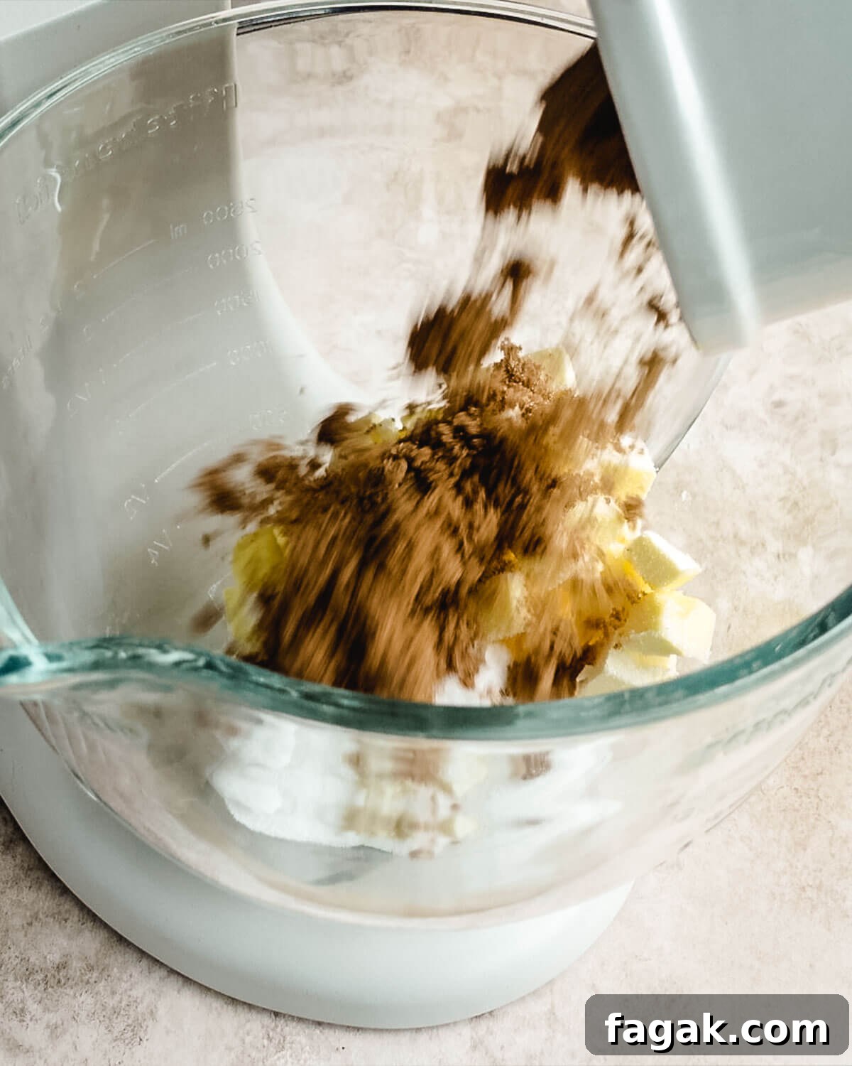 Brown sugar being added to a glass Kitchenaid mixing bowl of butter.