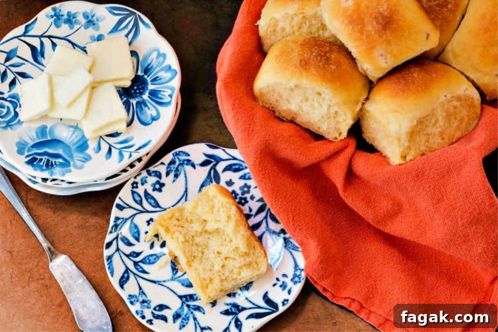 Overhead shot of a basket of potato rolls, a plate with slices of butter, and a plate with a split cheese roll.