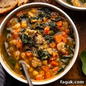 A white bowl with Italian sausage soup in it arranged on a wooden board with another bowl of soup and slices of sourdough bread next to it.
