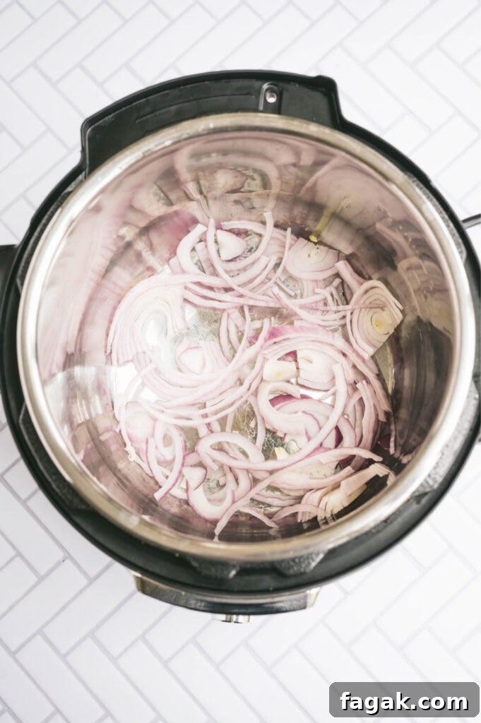 Overhead photo of red onion sauteing in the instant pot on a white tile surface.
