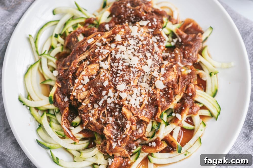 Close up photo of zoodles topped with Instant Pot Balsamic chicken, sprinkled with parmesan cheese. These are on a white plate with a gray linen background.