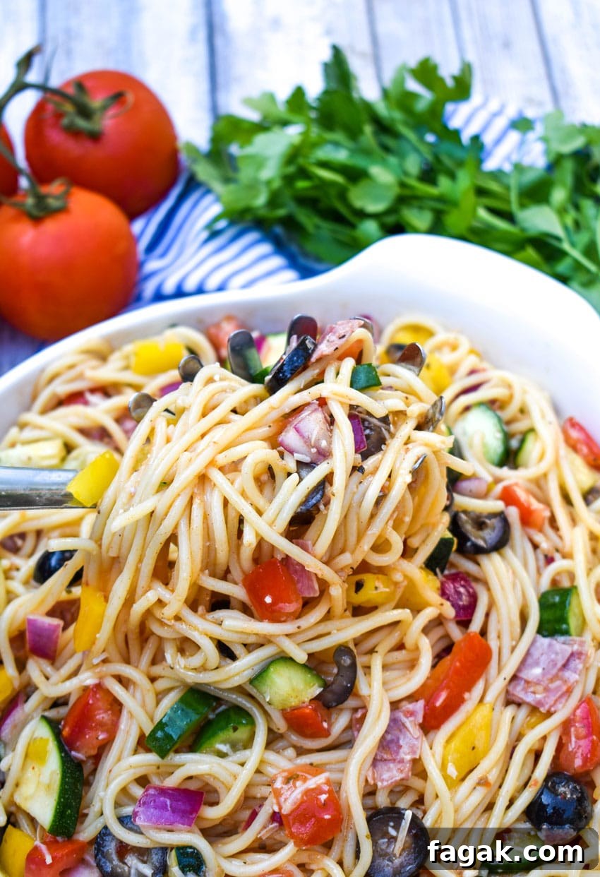 summer spaghetti salad being lifted out of a white bowl by a silver serving spoon