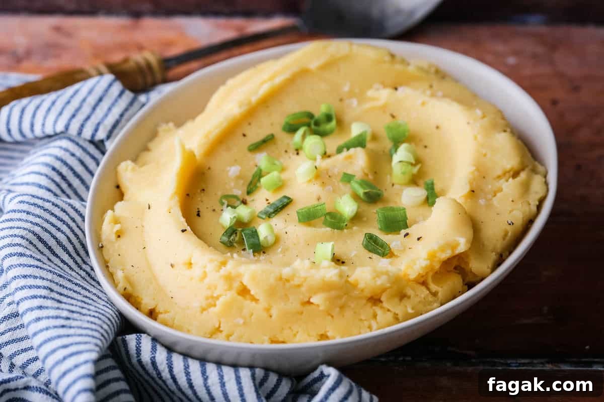 A bowl of cheesy mashed potatoes sprinkled with spring onions and flaked sea salt.
