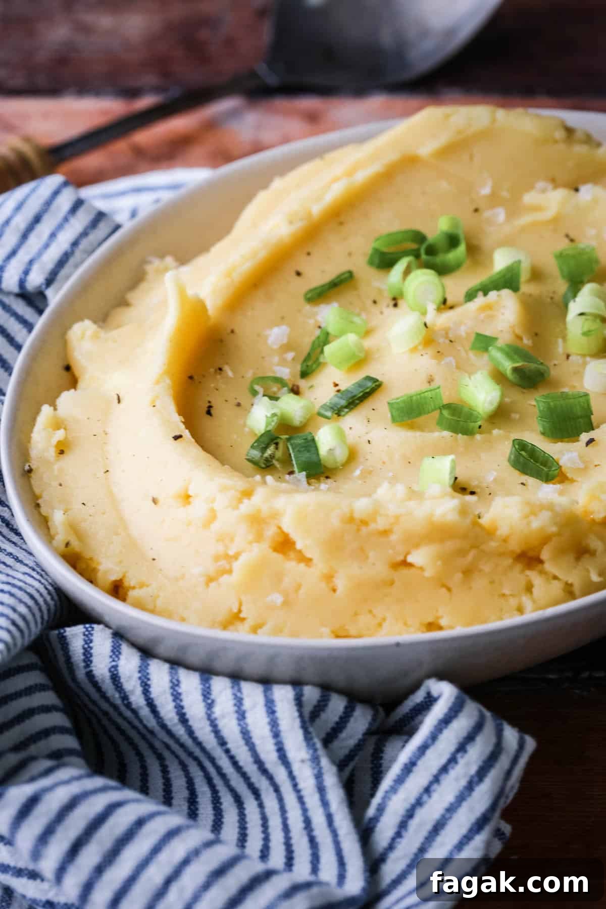 A bowl of cheesy mashed potatoes sprinkled with spring onions and flaked sea salt.