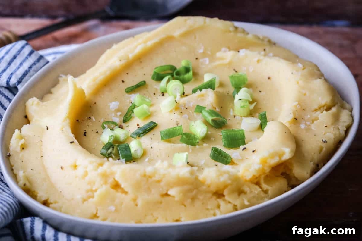 A bowl of cheesy mashed potatoes sprinkled with spring onions and flaked sea salt.