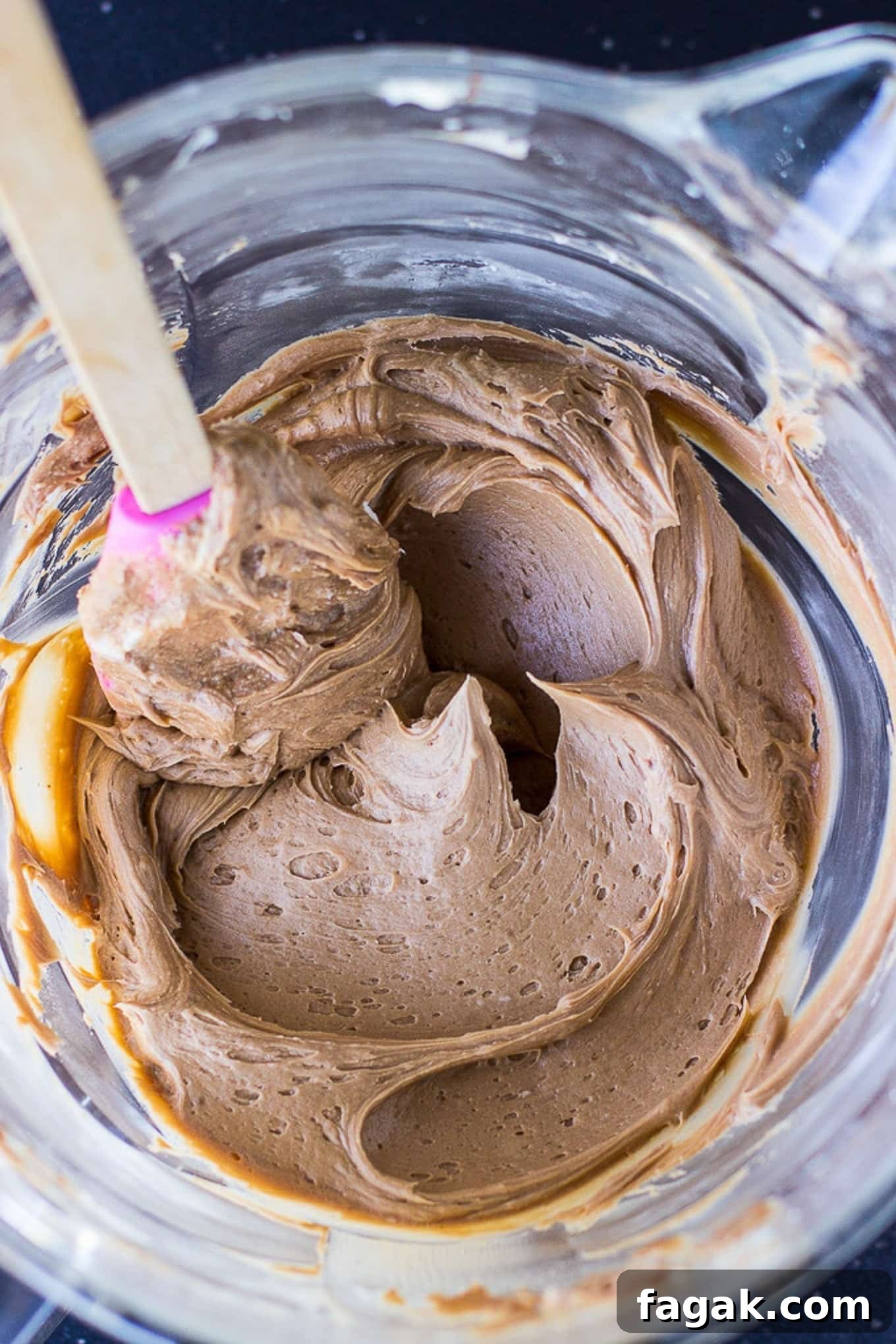 Chocolate frosting in a glass bowl with a spatula stirring it around.