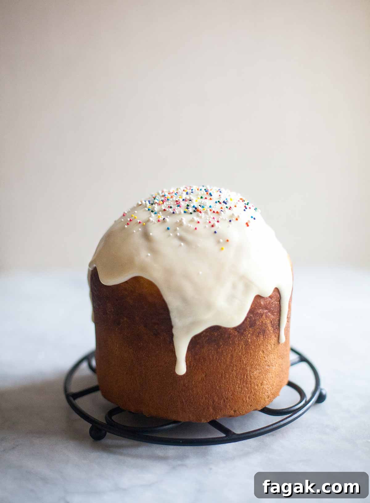 A loaf of kulich topped with glaze and sprinkles on a round trivet