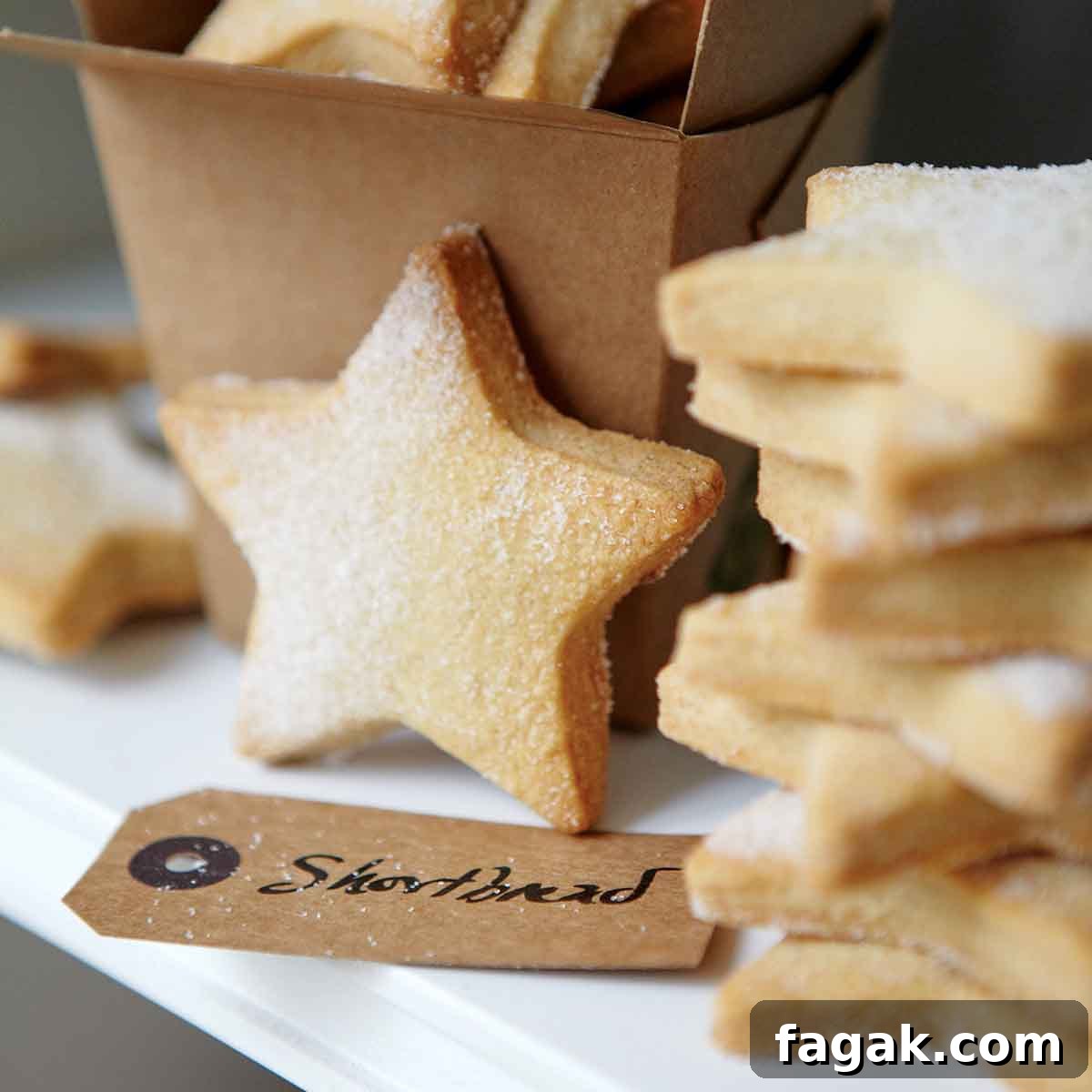A stack of star-shaped cutout classic shortbread cookies, lightly dusted with sugar, and a brown takeout container and a gift tag.