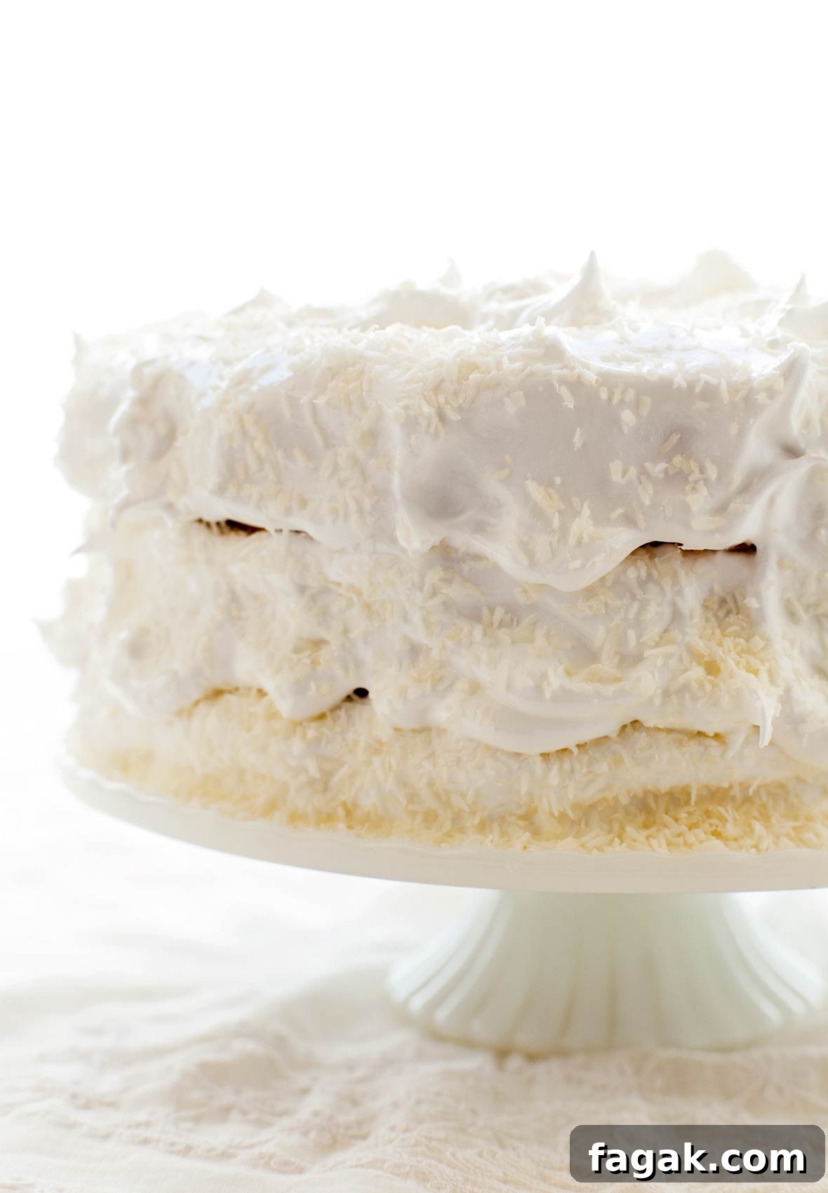 A 3-layer coconut angel food cake covered in white frosting on a white cake stand