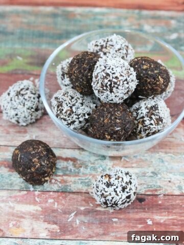 Chocolate coconut energy balls with dates in a glass bowl with three energy balls beside the bowl and coconut around it.