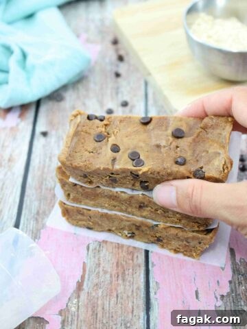 image of three cookie dough protein bars stacked with parchment paper between them and a hand placing the top one.