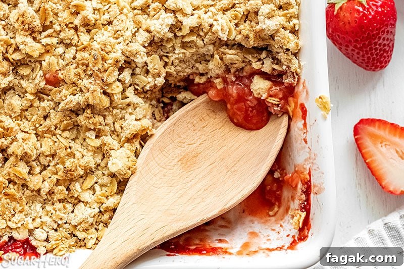 Wooden spoon scooping out Strawberry Crisp from the baking pan.