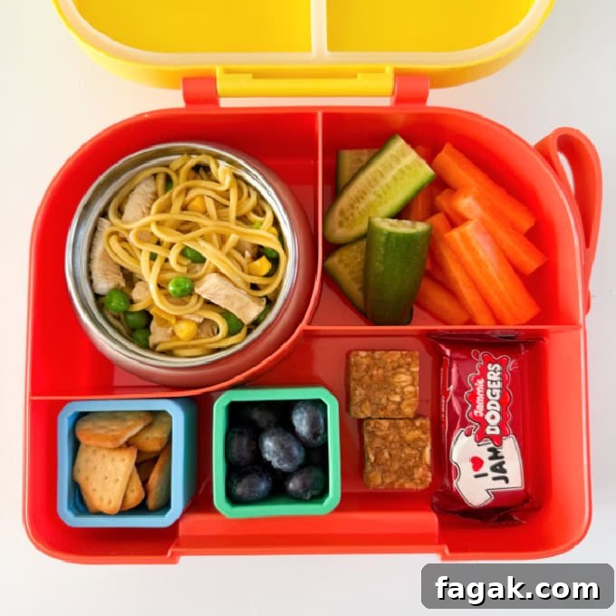 Chicken noodles served in a hot &  cold lunch box with sliced carrots and cucumber.