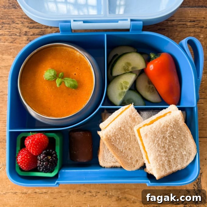 Airfryer Tomato Soup served in a bright blue hot & cold lunchbox with chopped cucumber, peppers and a cheese sandwich cut into squares.
