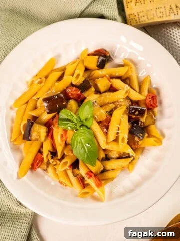 Pasta with eggplant and cherry tomatoes in a bowl garnished with fresh basil.