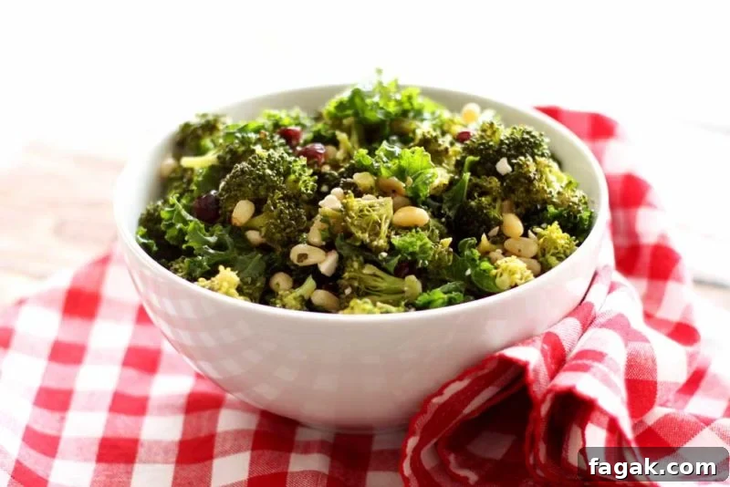 White bowl containing broccoli and kale salad with pine nuts and feta cheese on tip, sitting on a red and white gingham napkin.