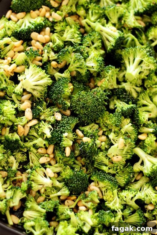Sheet pan containing broccoli spears with pine nuts and fresh ground pepper.
