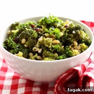 White bowl containing broccoli and kale salad with pine nuts and feta cheese on top, sitting on a red and white gingham napkin.