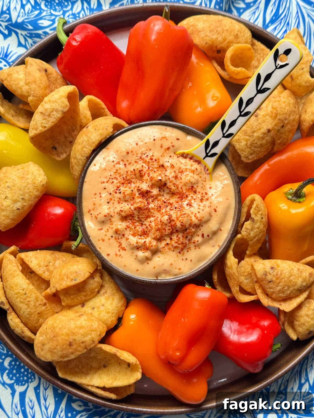 a bowl of corn dip set on a platter with mini peppers and Frito scoops