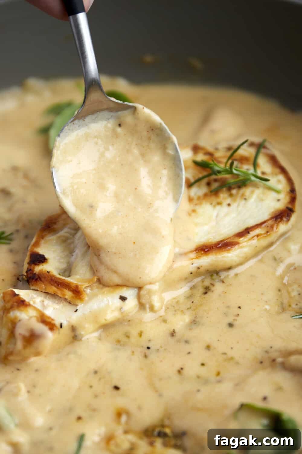 creamy parmesan sauce being spooned over a cooked chicken breast in a skillet