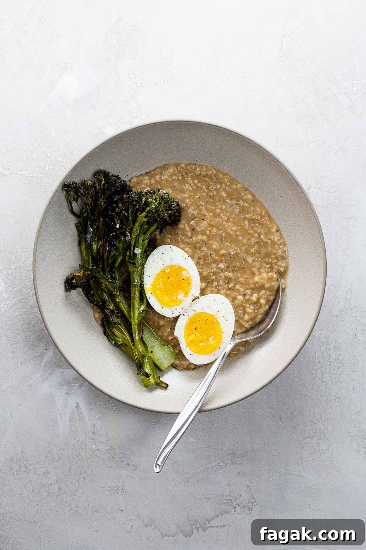 savory steel cut oats with a seven minute egg and crispy broccolini in a bowl with a spoon