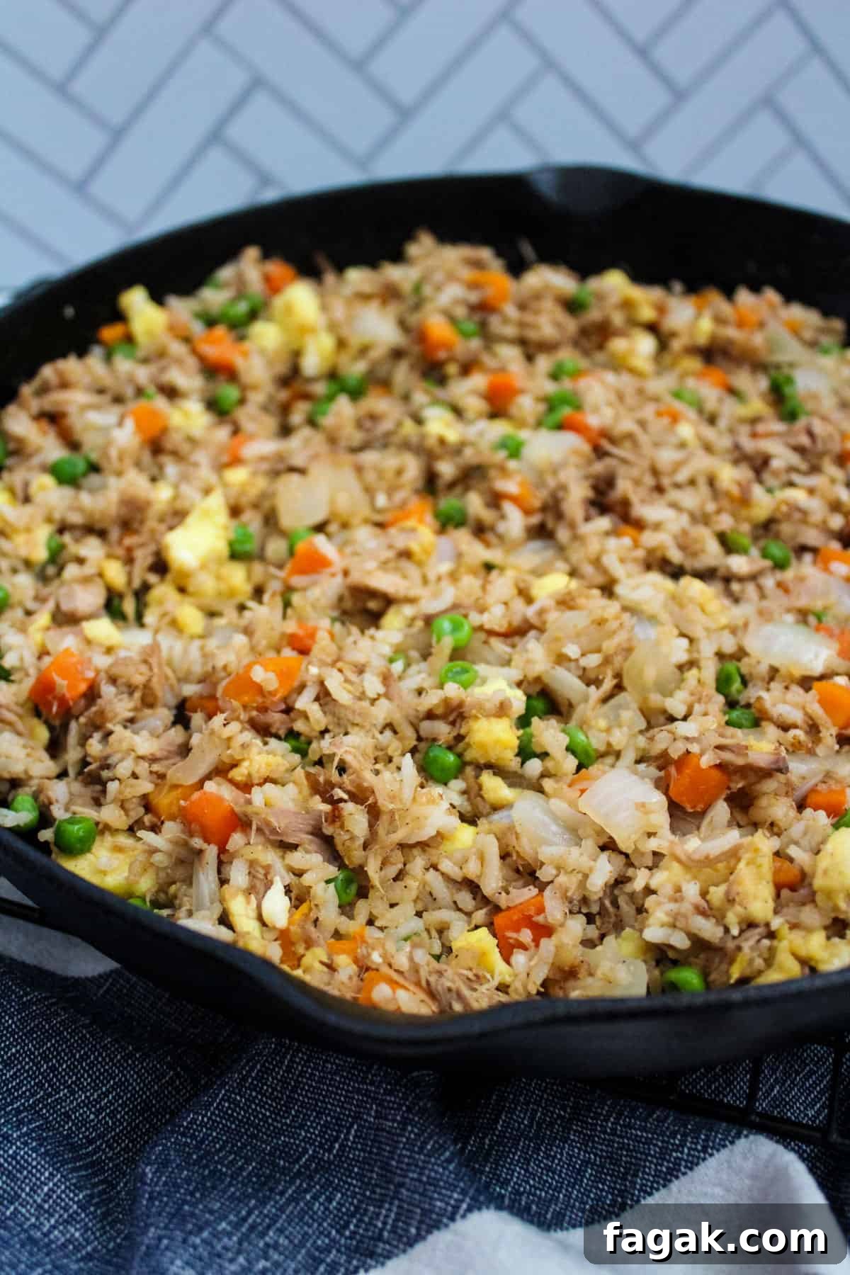 A cast iron skillet full of fried rice with onion, peas, carrots, eggs, and pulled pork.