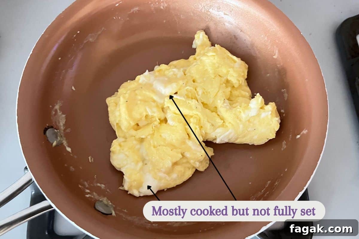 Scrambled eggs in a small skillet with a label that reads "mostly cooked but not fully set".