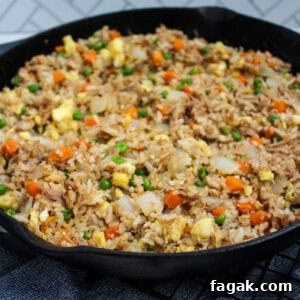 A cast iron skillet full of fried rice with onion, peas, carrots, eggs, and pulled pork.