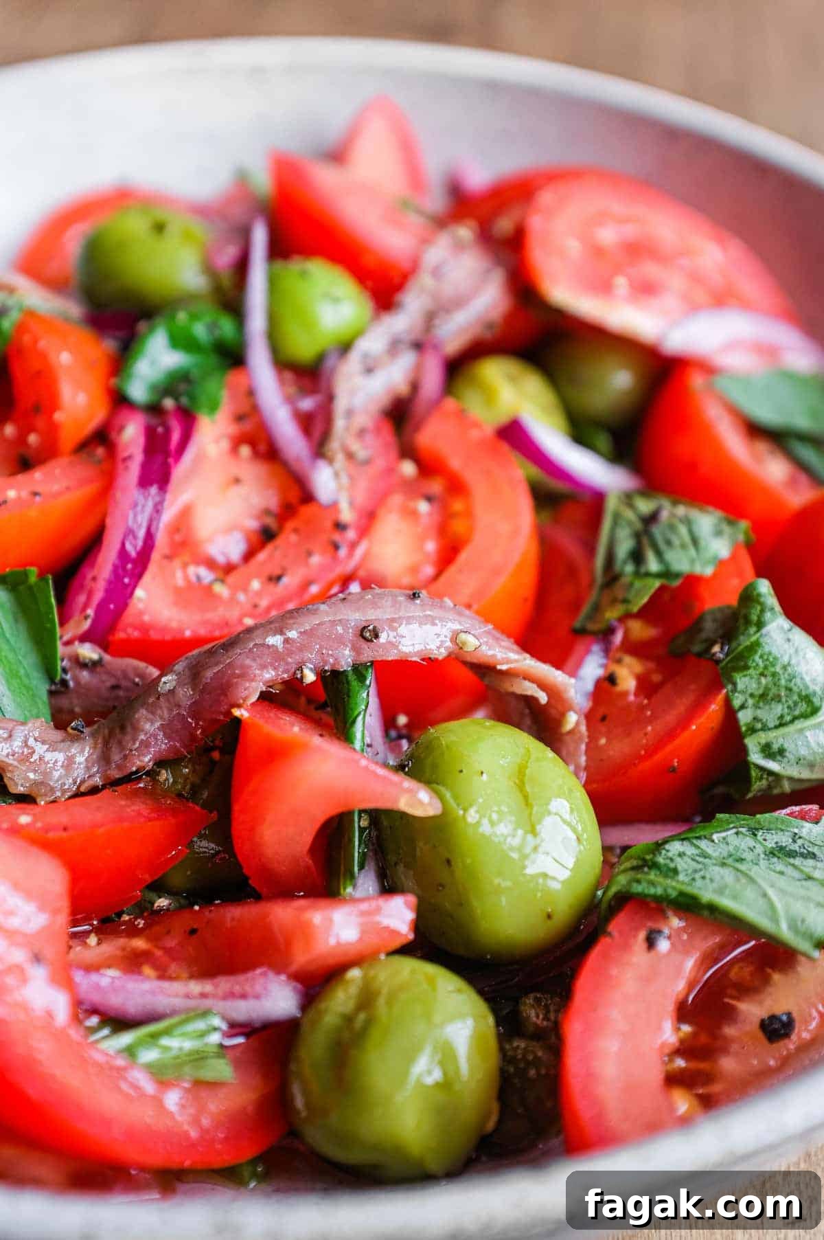 A bowl of Tomato salad with olives, capers, red onion, anchovies and fresh basil.