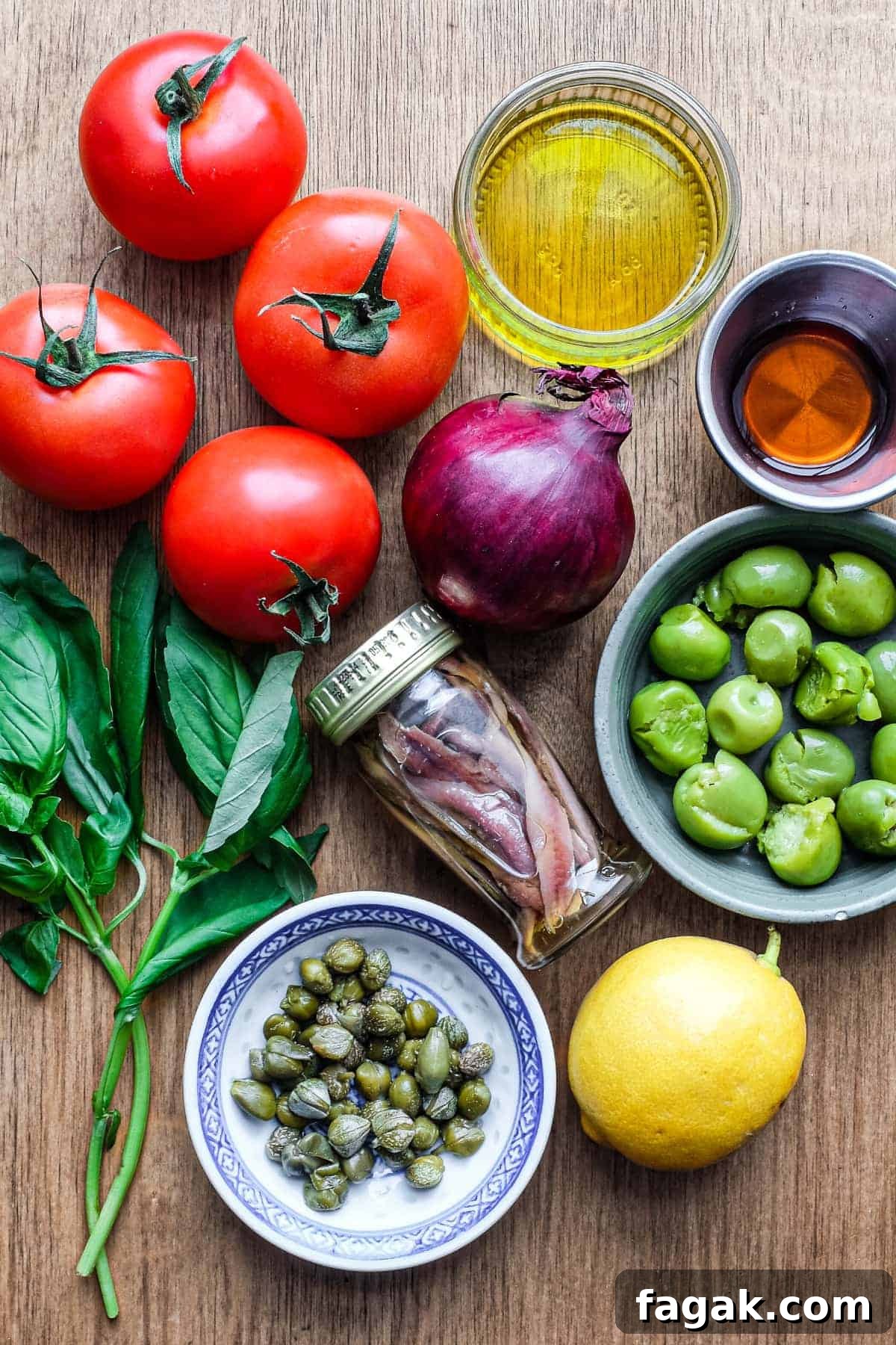 The ingredients for Aeloian Salad: tomatoes, red onion, red wine vinegar, lemon, green olives, anchovies, basil and extra virgin olive oil.