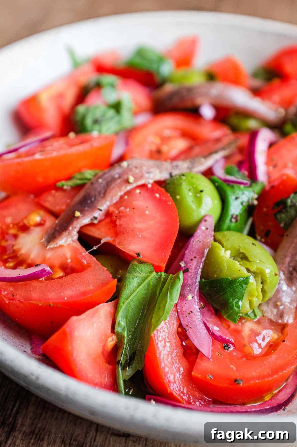 A bowl of Tomato salad with olives, capers, red onion, anchovies and fresh basil.